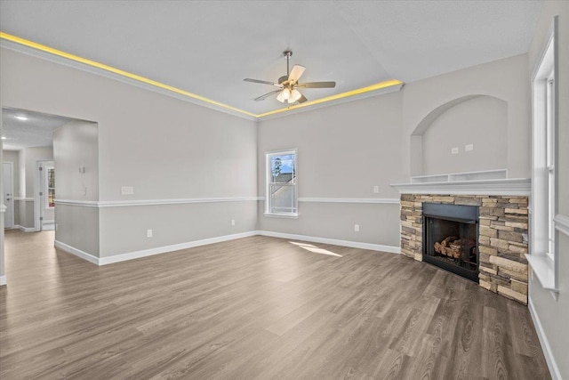 unfurnished living room featuring ceiling fan, a stone fireplace, wood finished floors, and baseboards