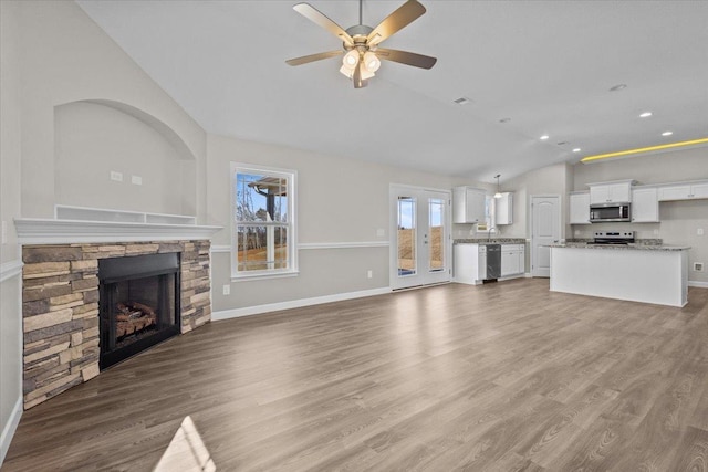 unfurnished living room with a stone fireplace, recessed lighting, baseboards, vaulted ceiling, and light wood-style floors