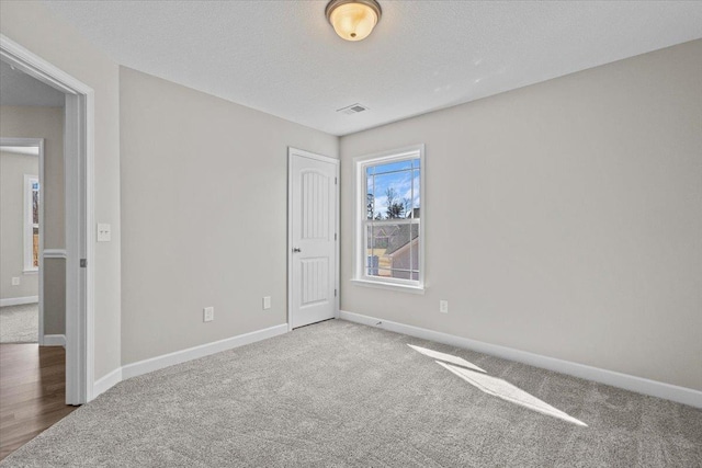 carpeted spare room featuring a textured ceiling, visible vents, and baseboards