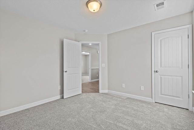 unfurnished bedroom with carpet, visible vents, a textured ceiling, and baseboards