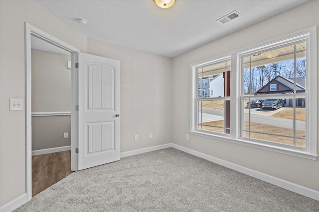 unfurnished bedroom with carpet floors, visible vents, a textured ceiling, and baseboards