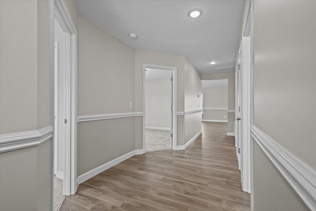 hall featuring a textured ceiling, recessed lighting, wood finished floors, and baseboards