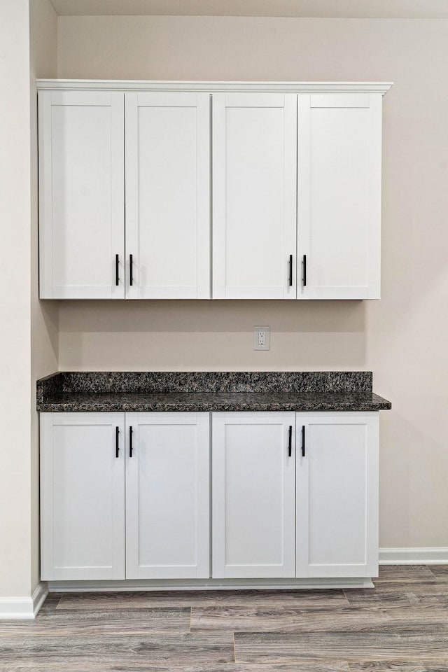 bar featuring dark stone countertops, light hardwood / wood-style flooring, and white cabinets