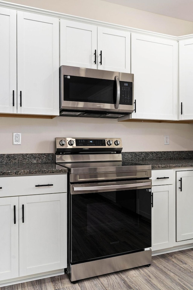 kitchen with dark stone countertops, appliances with stainless steel finishes, white cabinetry, and light hardwood / wood-style floors