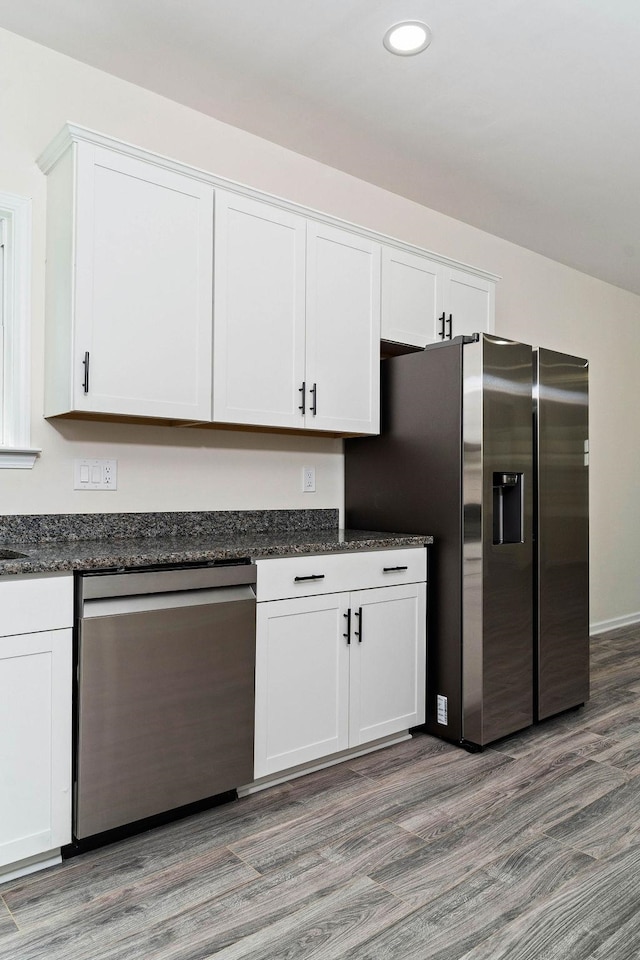 kitchen featuring stainless steel appliances, dark stone counters, light wood-type flooring, and white cabinets