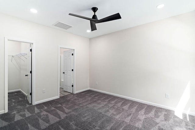 unfurnished bedroom featuring dark carpet, ceiling fan, a walk in closet, and a closet