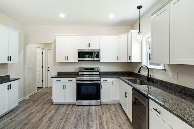 kitchen featuring pendant lighting, hardwood / wood-style floors, appliances with stainless steel finishes, sink, and white cabinets