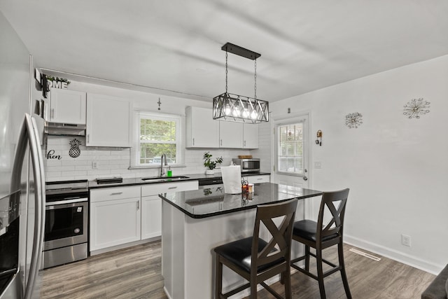 kitchen featuring a kitchen island, decorative light fixtures, appliances with stainless steel finishes, and white cabinetry