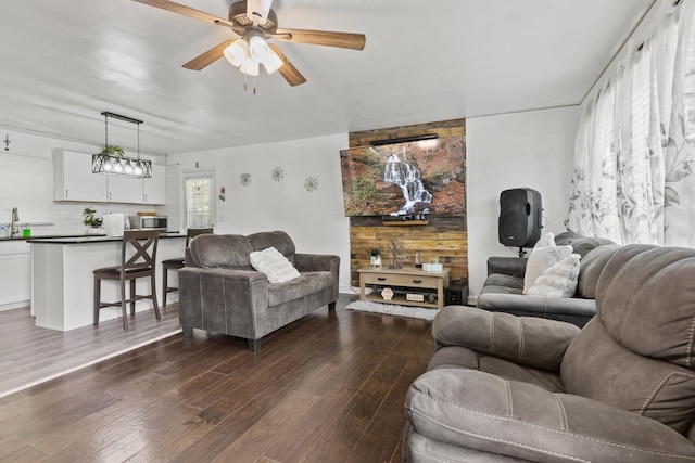 living room with sink, ceiling fan with notable chandelier, wooden walls, and dark hardwood / wood-style flooring