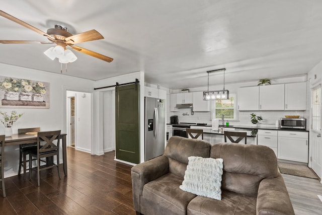 living room with dark wood-type flooring, sink, ceiling fan, and a barn door