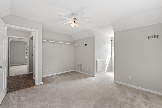 unfurnished bedroom with a textured ceiling, a closet, lofted ceiling, light colored carpet, and ceiling fan