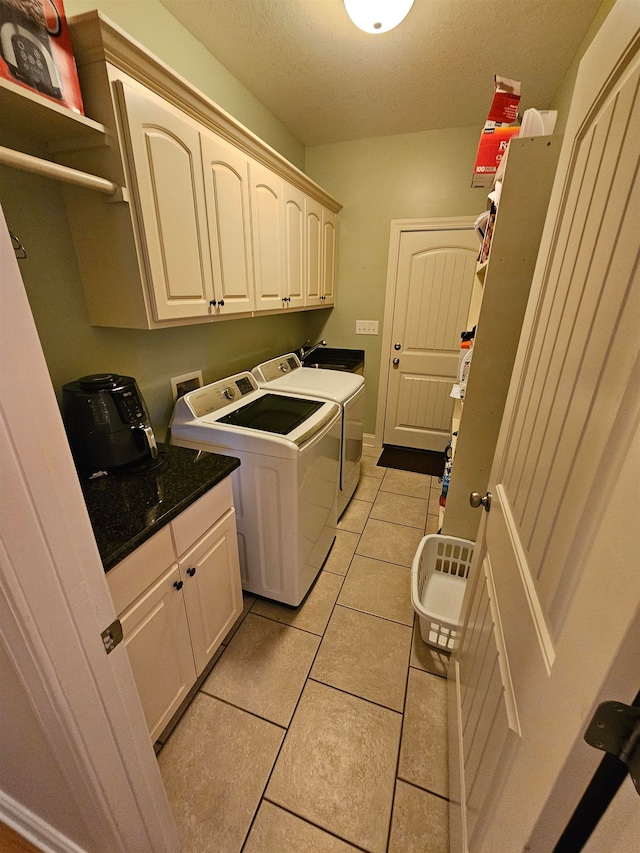 clothes washing area featuring light tile patterned floors, a textured ceiling, cabinets, and washing machine and dryer