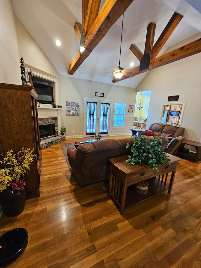 living room with high vaulted ceiling, ceiling fan, a stone fireplace, hardwood / wood-style flooring, and beam ceiling