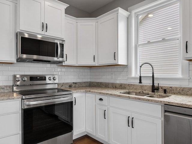 kitchen with appliances with stainless steel finishes, white cabinetry, sink, and light stone countertops