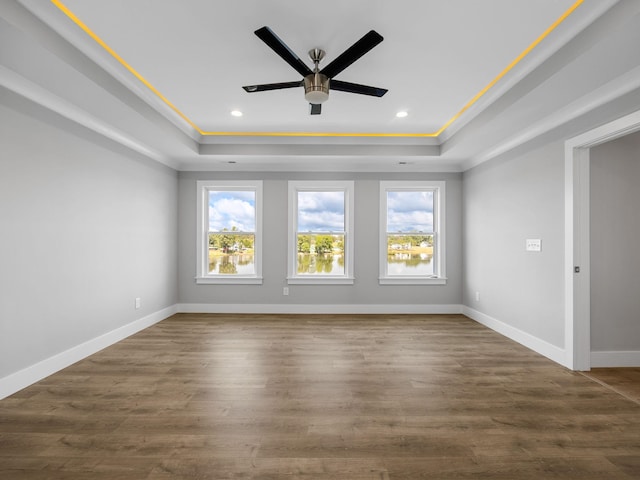 empty room with crown molding, dark wood-type flooring, ceiling fan, and a tray ceiling