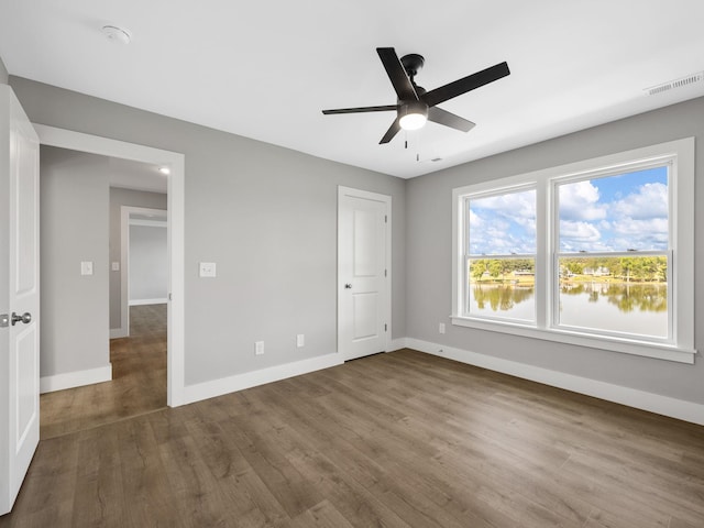 unfurnished bedroom with ceiling fan, hardwood / wood-style floors, and a water view