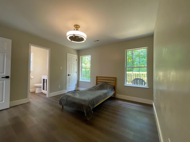 bedroom with multiple windows, ensuite bathroom, and dark hardwood / wood-style floors