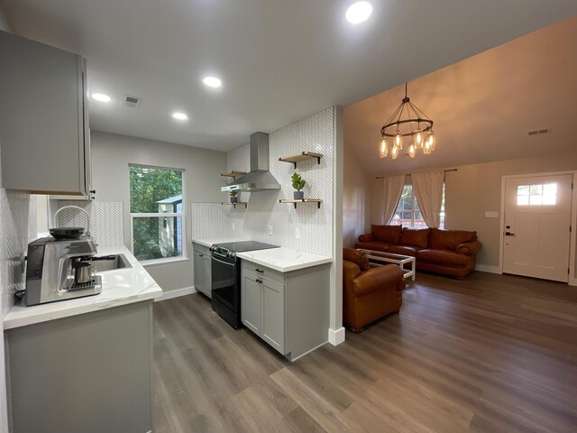 kitchen featuring dark hardwood / wood-style flooring, black electric range, pendant lighting, a notable chandelier, and wall chimney range hood