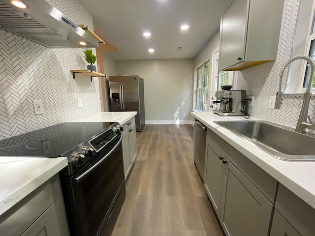 kitchen featuring wall chimney exhaust hood, hardwood / wood-style floors, tasteful backsplash, stainless steel appliances, and sink