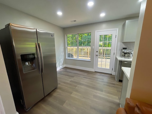 kitchen featuring stainless steel fridge, decorative backsplash, white cabinetry, and light hardwood / wood-style floors