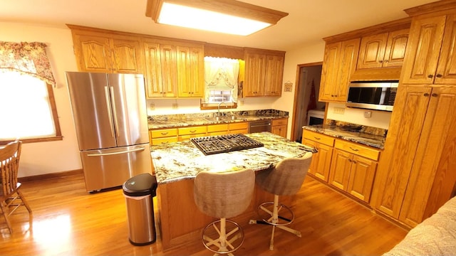 kitchen with a sink, light wood-type flooring, a kitchen island, and appliances with stainless steel finishes