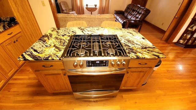 interior details with light wood-type flooring, light stone countertops, stainless steel range with gas stovetop, and brown cabinetry