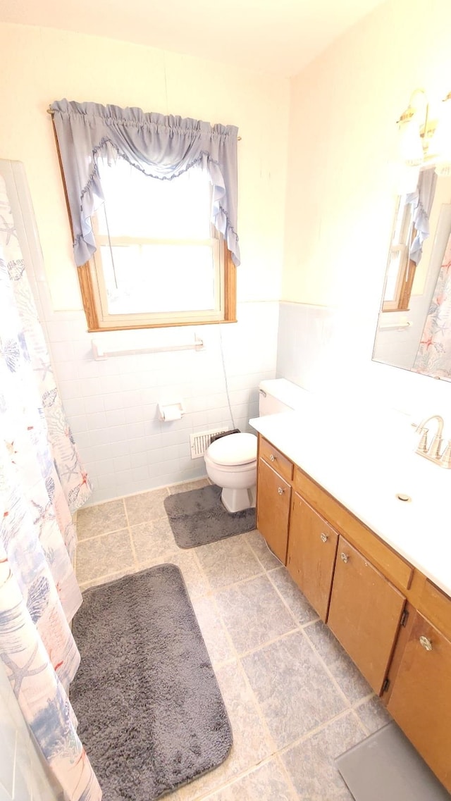 bathroom with vanity, tile walls, toilet, and a wainscoted wall