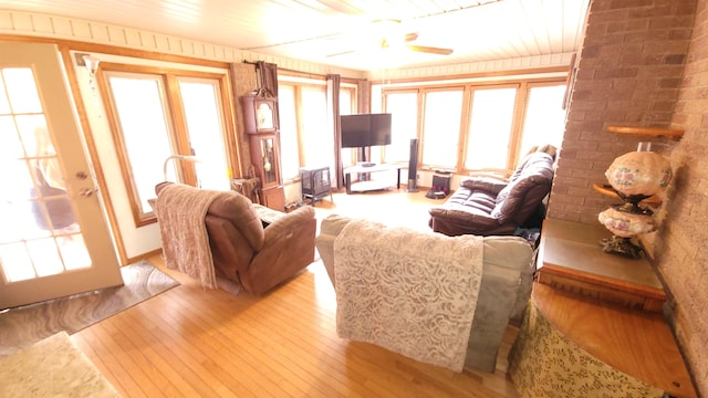 living area featuring light wood-style flooring, brick wall, and a ceiling fan