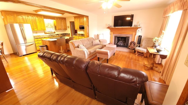 living room featuring ceiling fan, plenty of natural light, light wood-style floors, and a fireplace with raised hearth