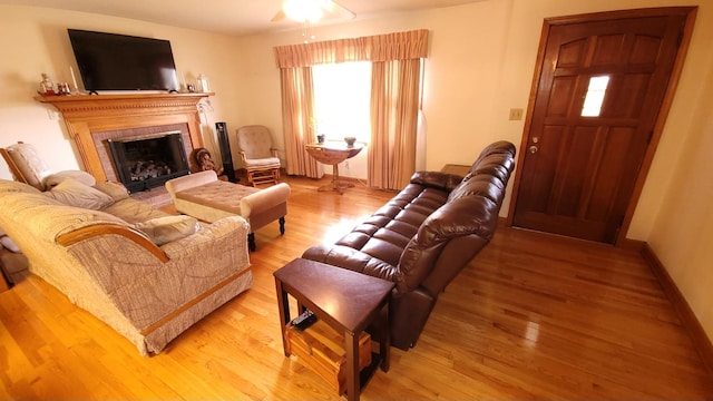 living area featuring baseboards, a fireplace with flush hearth, light wood-style floors, and a ceiling fan