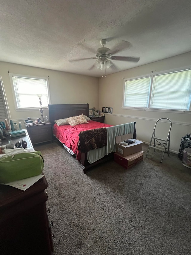 bedroom featuring multiple windows, a textured ceiling, dark carpet, and ceiling fan