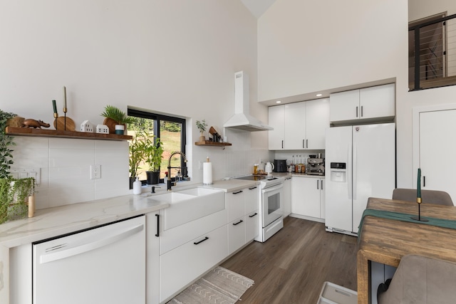 kitchen with white cabinets, white appliances, sink, wall chimney range hood, and a towering ceiling