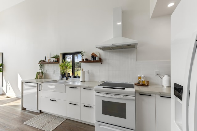 kitchen with white range, wall chimney exhaust hood, light hardwood / wood-style flooring, decorative backsplash, and white cabinetry