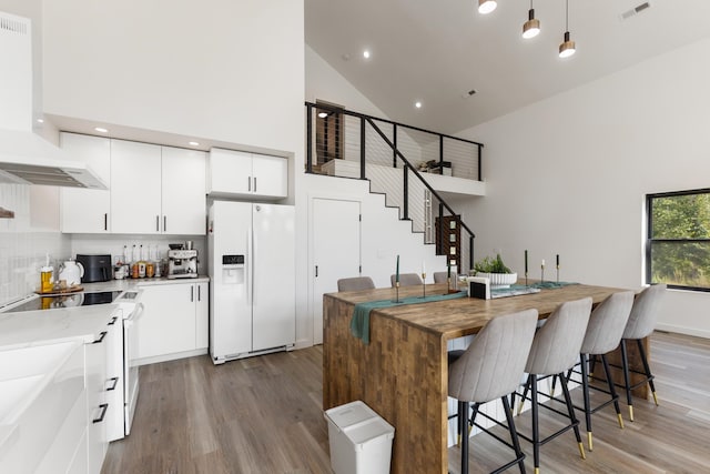 kitchen with high vaulted ceiling, decorative light fixtures, exhaust hood, and white refrigerator with ice dispenser