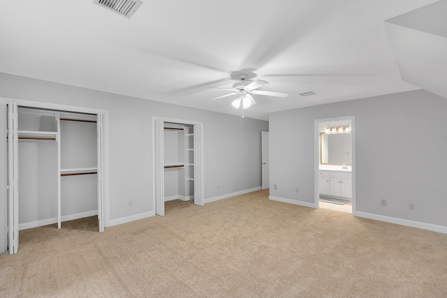 unfurnished bedroom featuring ensuite bath, ceiling fan, multiple closets, light colored carpet, and lofted ceiling