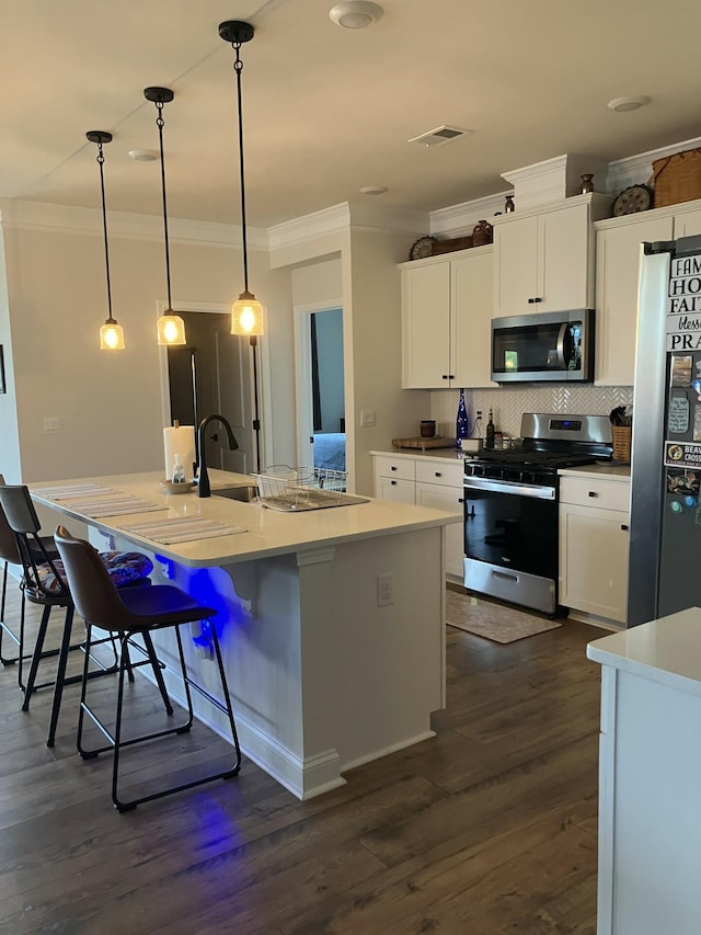 kitchen with white cabinets, appliances with stainless steel finishes, pendant lighting, and an island with sink