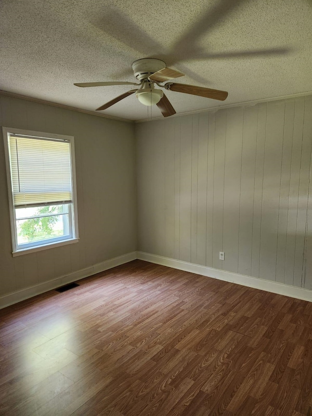 unfurnished room featuring wooden walls, ceiling fan, hardwood / wood-style flooring, and a textured ceiling