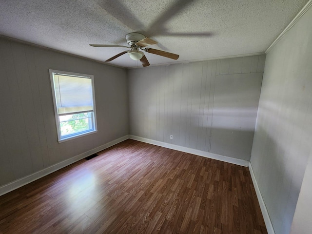 empty room featuring ceiling fan, a textured ceiling, wooden walls, dark wood-type flooring, and crown molding