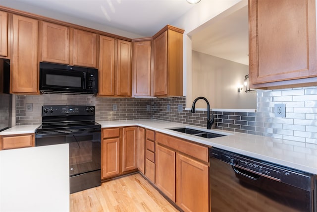 kitchen with light wood-type flooring, black appliances, tasteful backsplash, and sink