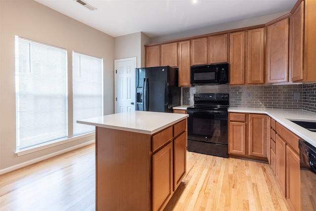 kitchen with black appliances, a kitchen island, decorative backsplash, and light hardwood / wood-style flooring