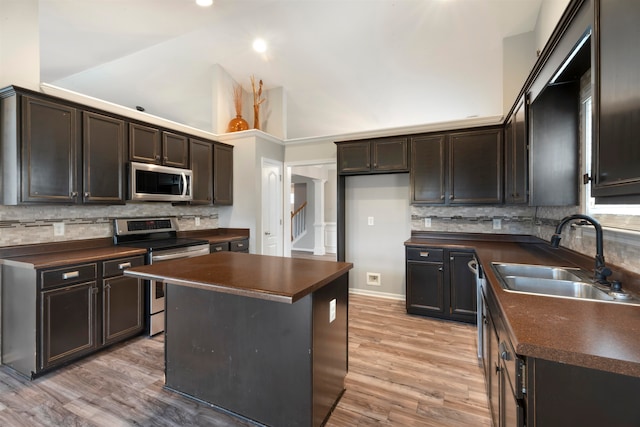 kitchen featuring appliances with stainless steel finishes, high vaulted ceiling, a kitchen island, light hardwood / wood-style flooring, and sink