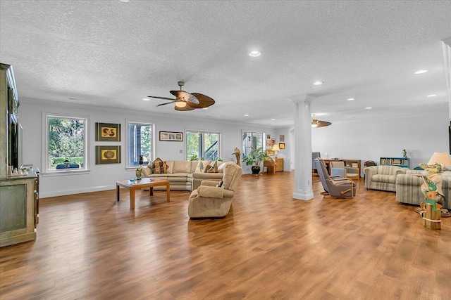 living room featuring a ceiling fan, wood finished floors, decorative columns, and a textured ceiling