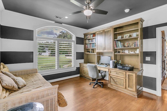 home office featuring crown molding, light wood-style floors, a ceiling fan, visible vents, and built in desk