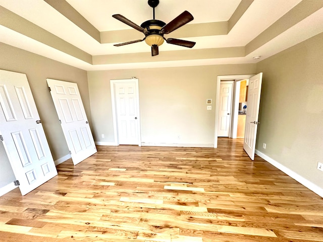 unfurnished bedroom featuring ceiling fan, light wood-type flooring, and a raised ceiling