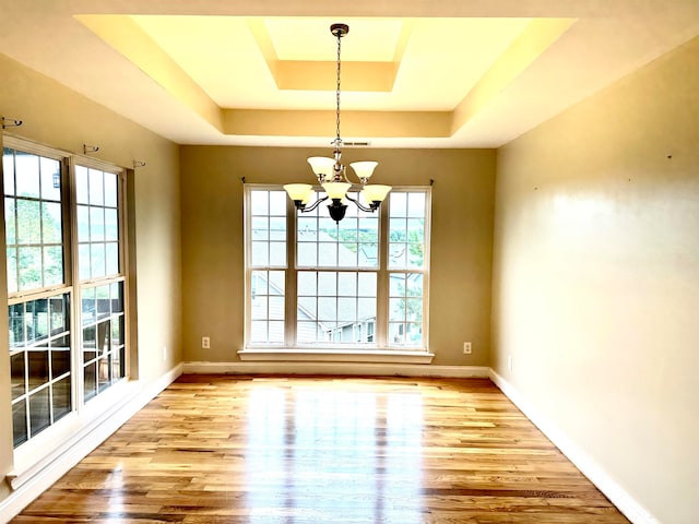 unfurnished room with an inviting chandelier, a raised ceiling, and light hardwood / wood-style floors