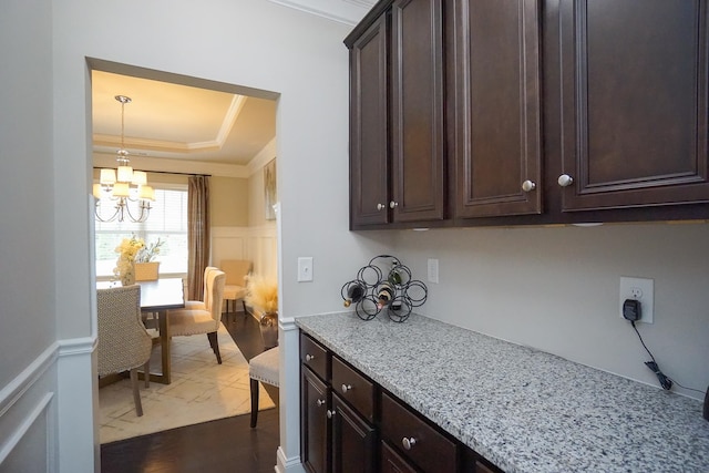 kitchen with dark brown cabinets, a tray ceiling, an inviting chandelier, crown molding, and light stone countertops