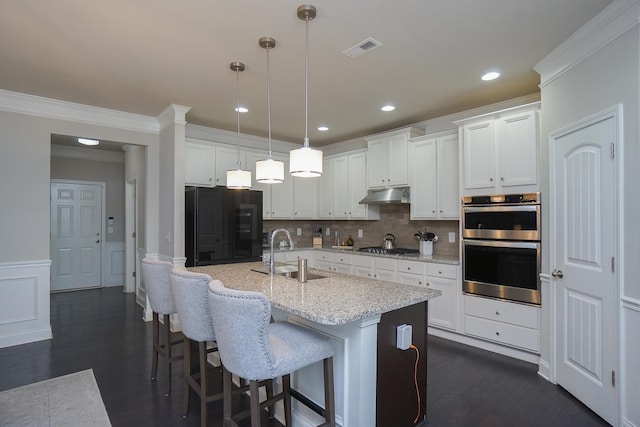 kitchen with white cabinets, stainless steel appliances, decorative light fixtures, a kitchen island with sink, and sink