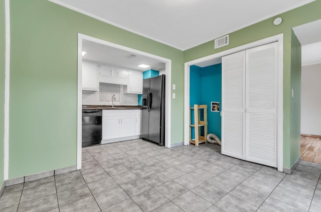 kitchen featuring tasteful backsplash, white cabinets, light tile patterned floors, black appliances, and crown molding