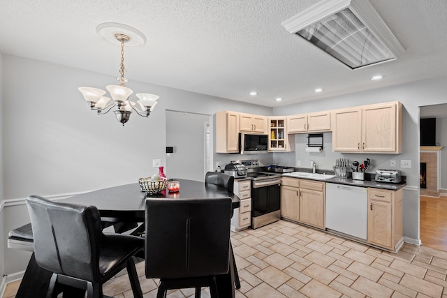 kitchen with appliances with stainless steel finishes, hanging light fixtures, light brown cabinets, sink, and a notable chandelier