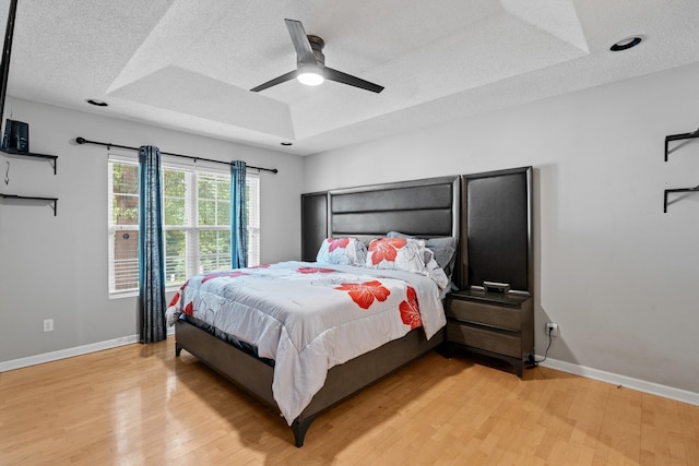 bedroom with ceiling fan, a textured ceiling, a raised ceiling, and light wood-type flooring